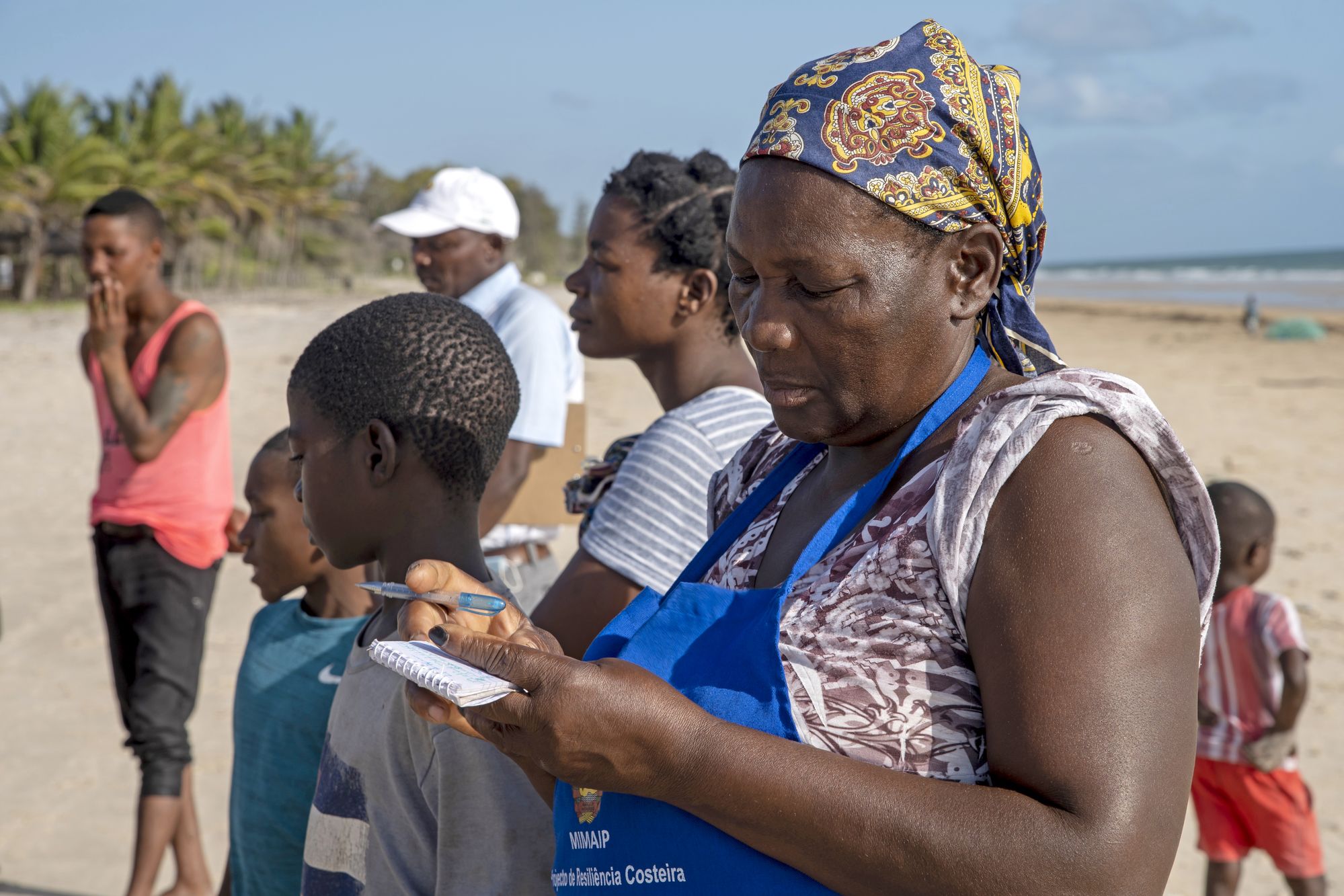 Eulália Baptista, a local fish merchant, taking notes and keeping track of what's being bought and sold as fishers sell their catch on the beach.