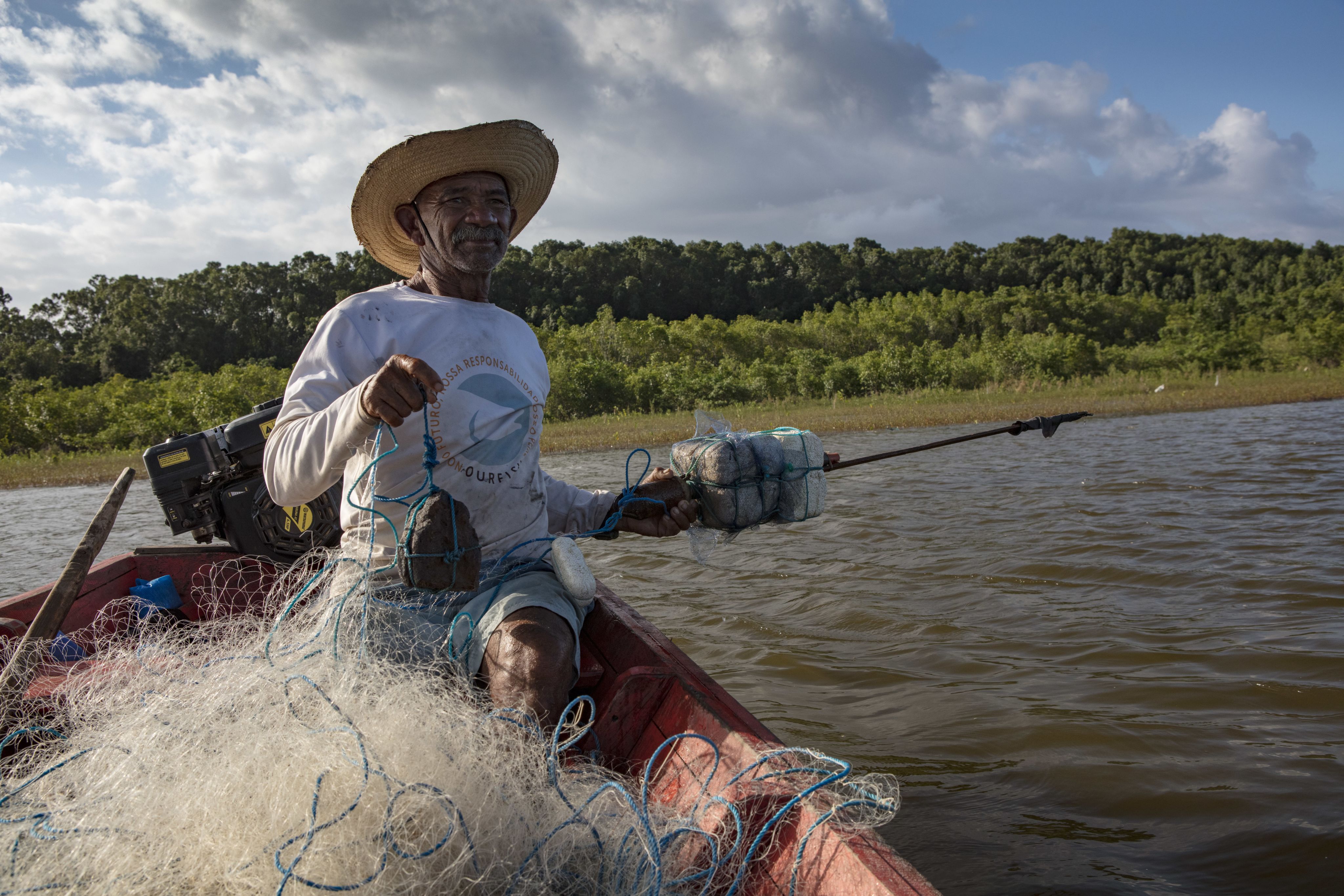 an old man wearing a hat and holding a rock anchor in a red small boat