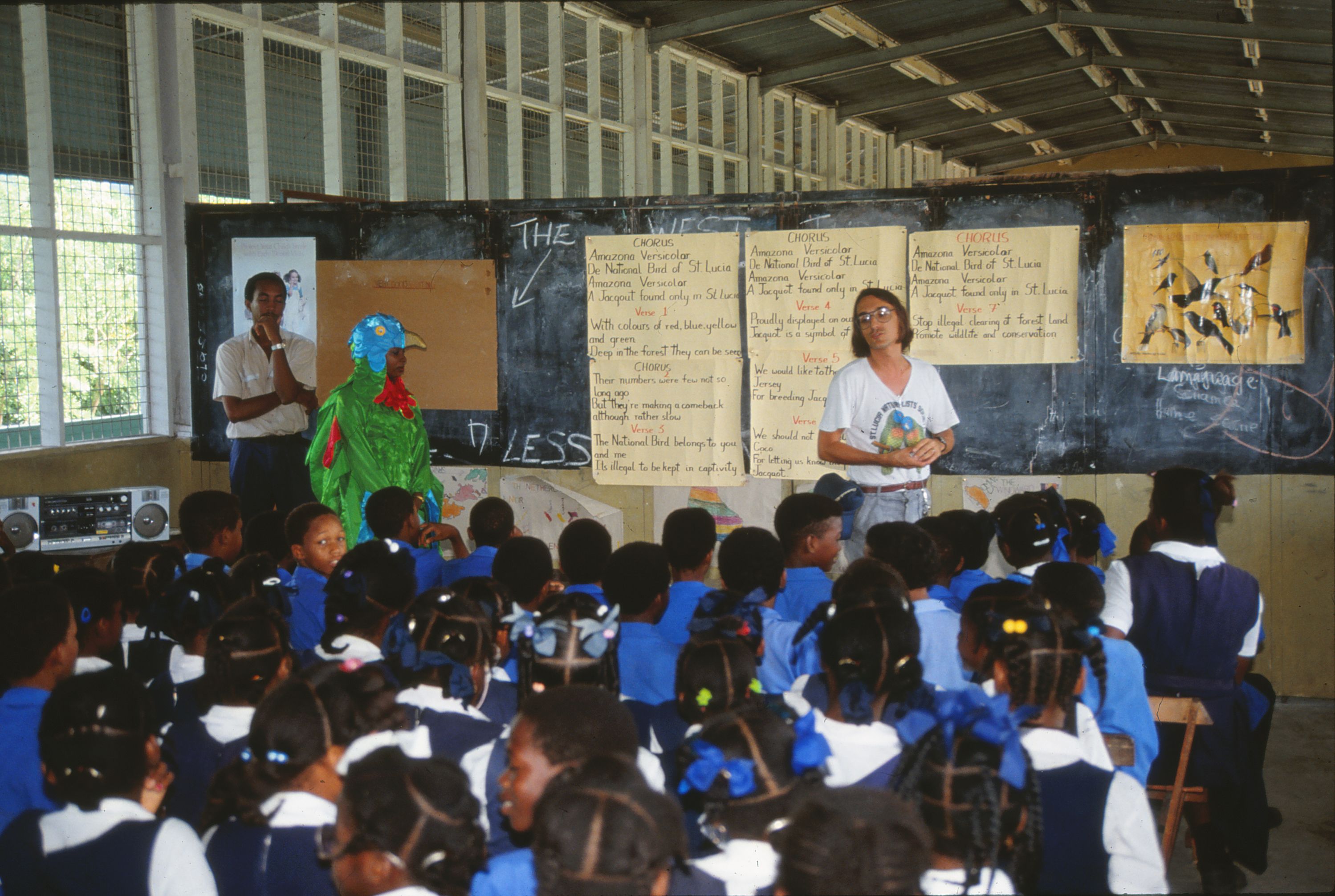 Photo of Paul Butler standing in front of a classroom in St. Lucia with a parrot mascot.
